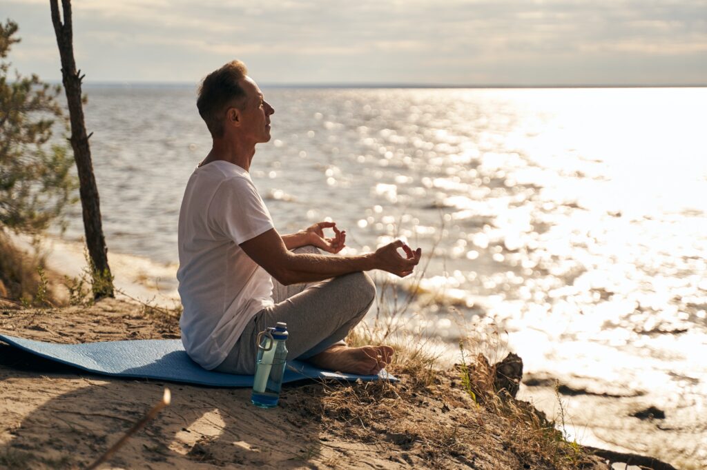 Calm mature man meditating on sea shore